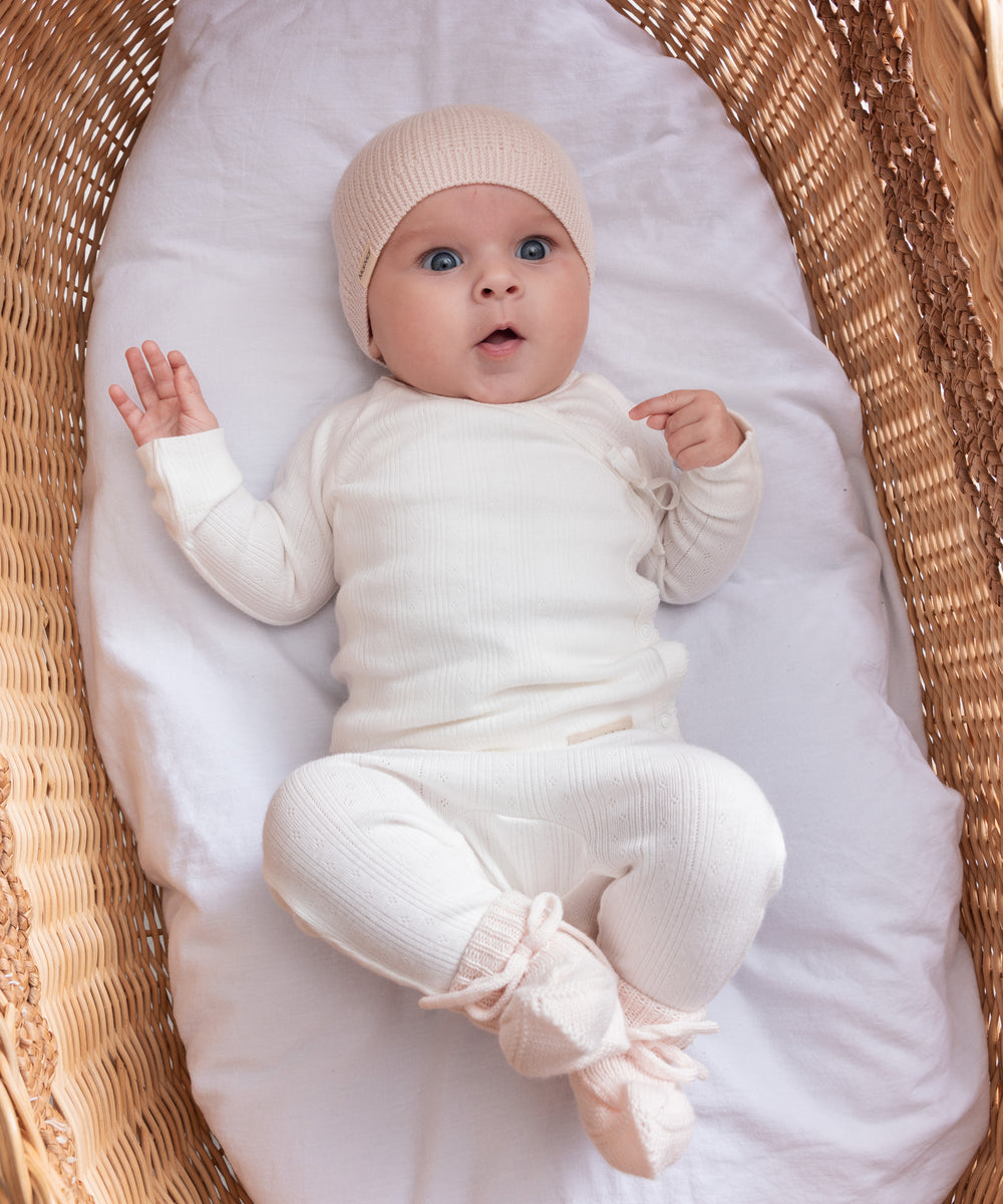 Baby iført hvide pointelle bukser og body liggende i en kurv