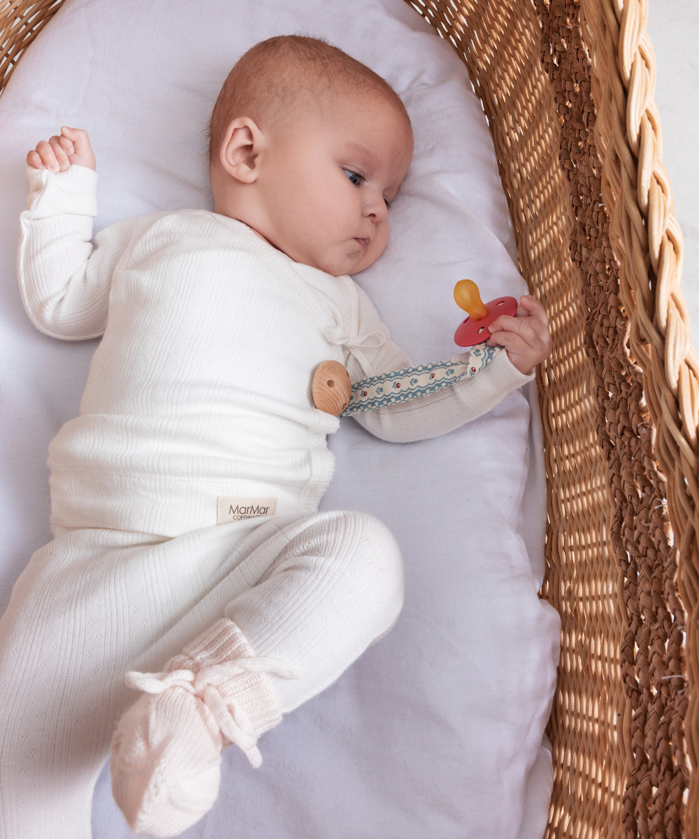 Baby iført hvide pointelle bukser og body liggende i en kurv