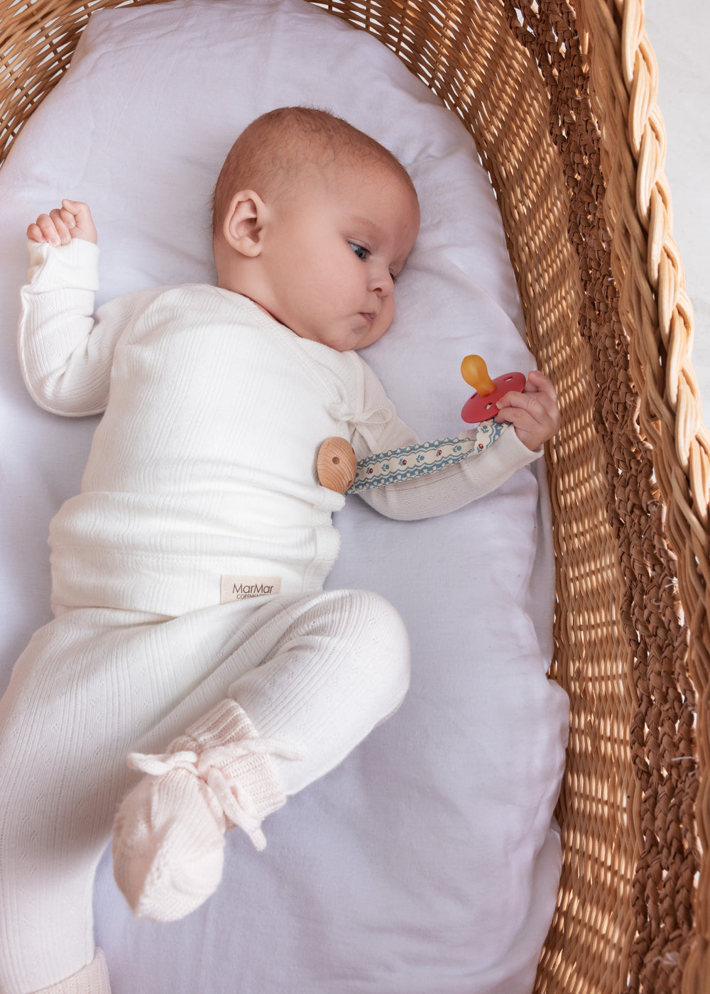 Baby iført hvide pointelle bukser og body liggende i en kurv