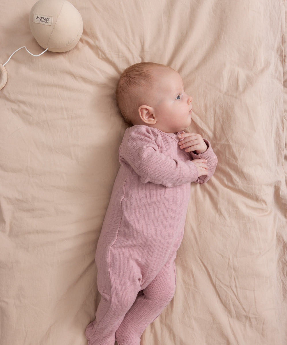 Baby iført rosa pointelle heldragt med fødder liggende på seng