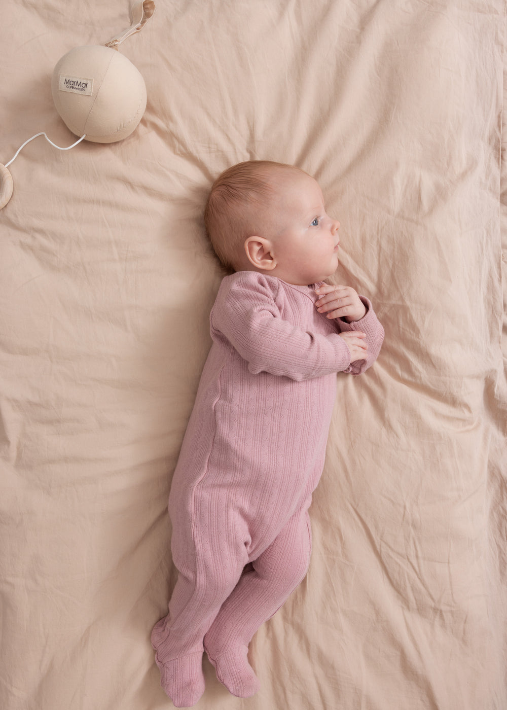 Baby iført rosa pointelle heldragt med fødder liggende på seng