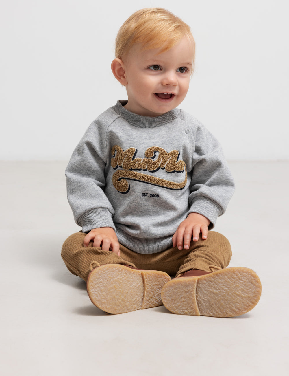 Sitting child in gray sweatshirt with gold embroidery