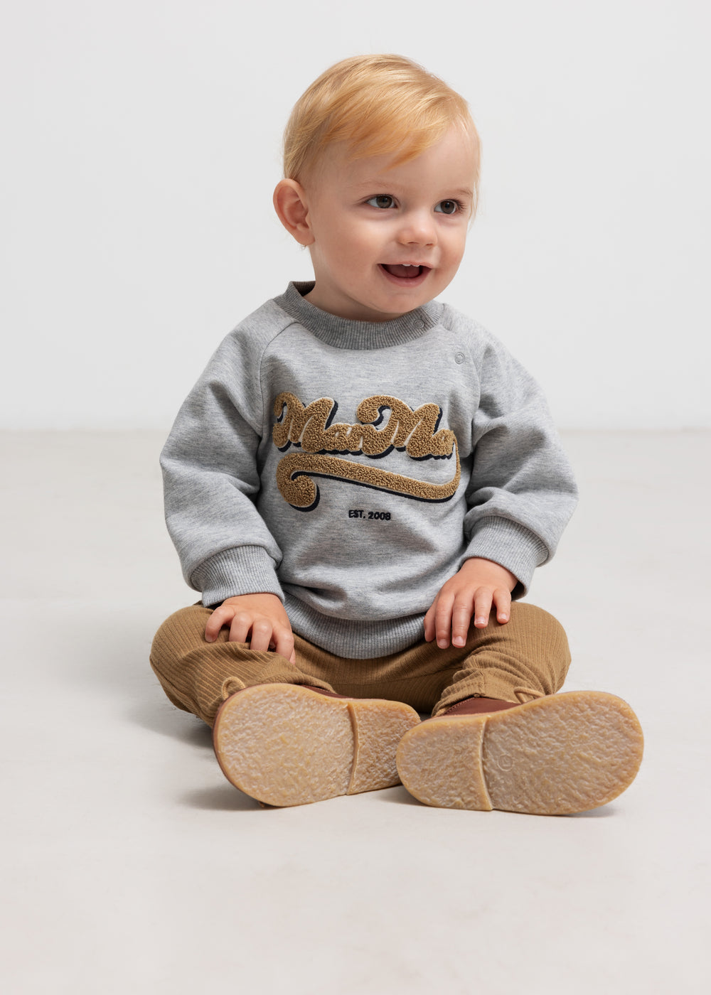 Baby iført brune ribstrikkede bukser och grå sweatshirt