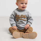 Baby iført brune ribstrikkede bukser och grå sweatshirt