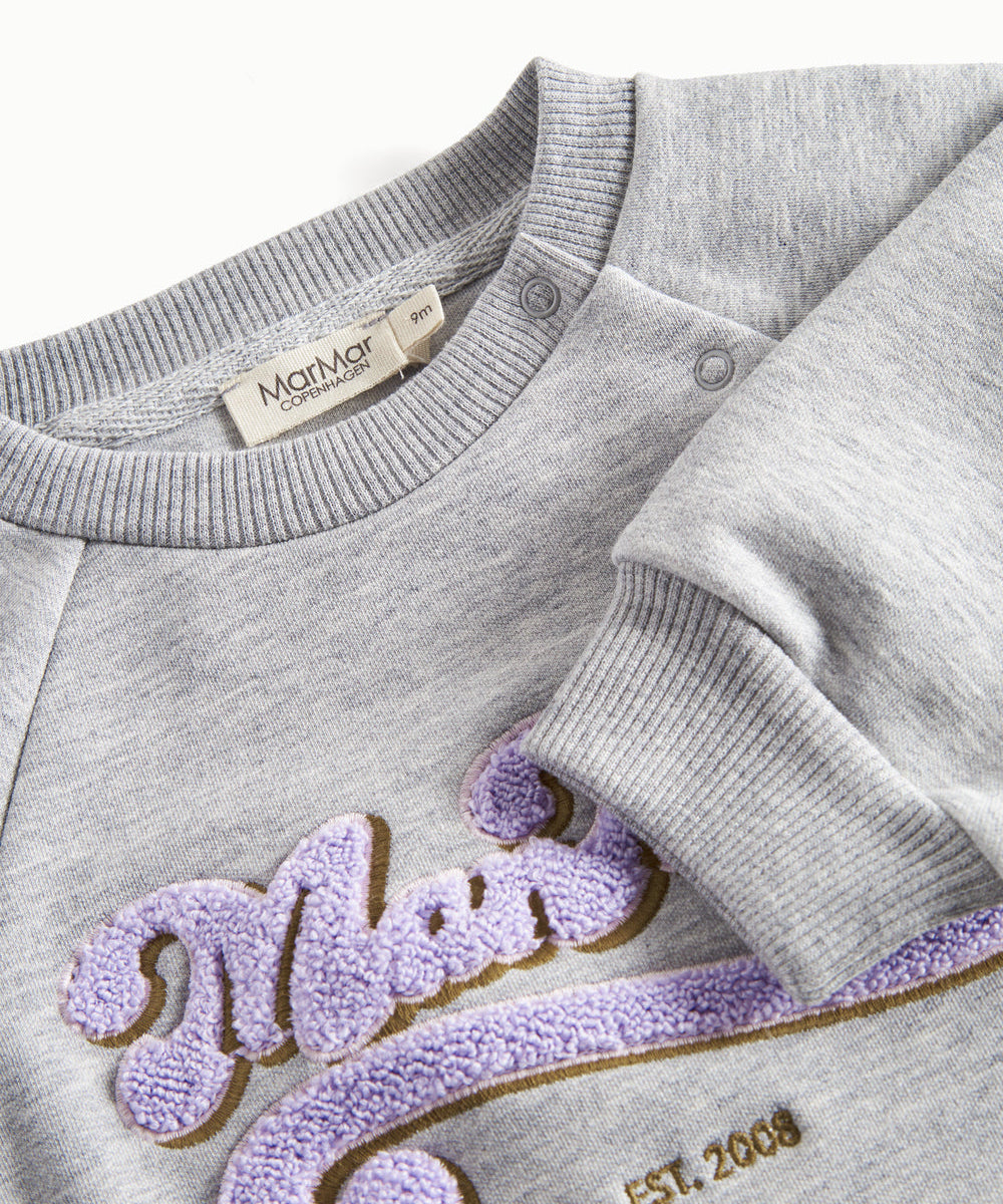 Nærbillede af broderi og ribkant på grå sweatshirt til børn