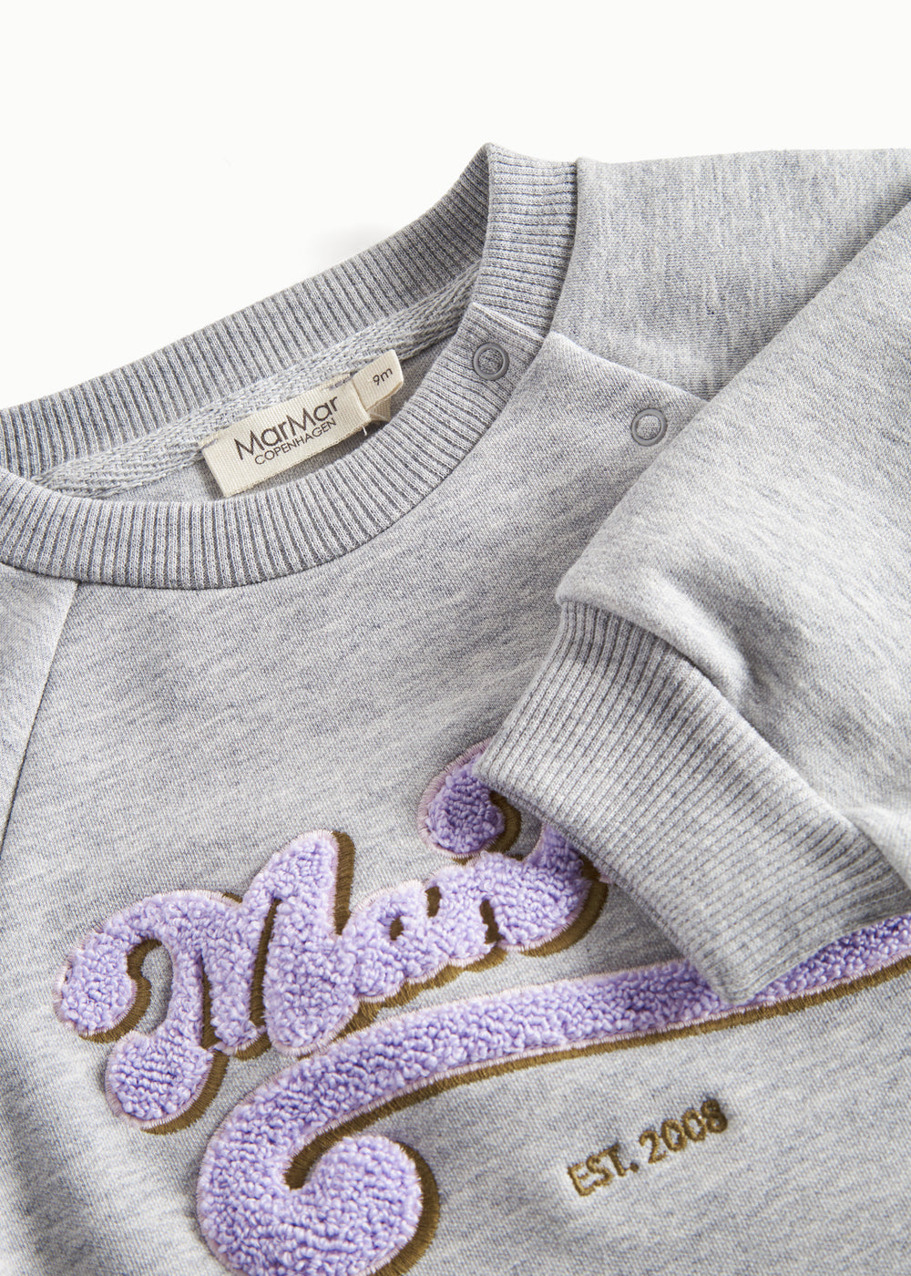 Nærbillede af broderi og ribkant på grå sweatshirt til børn