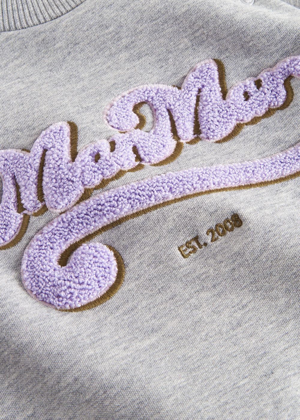 Detalje af lilla og guld broderi på grå sweatshirt til børn