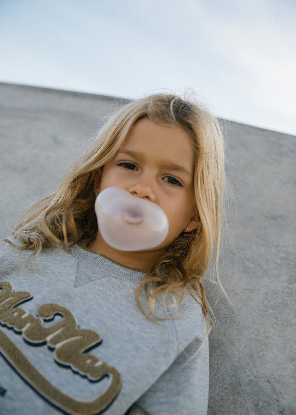 Børn med grå sweatshirt, der puster boble med tyggegummi