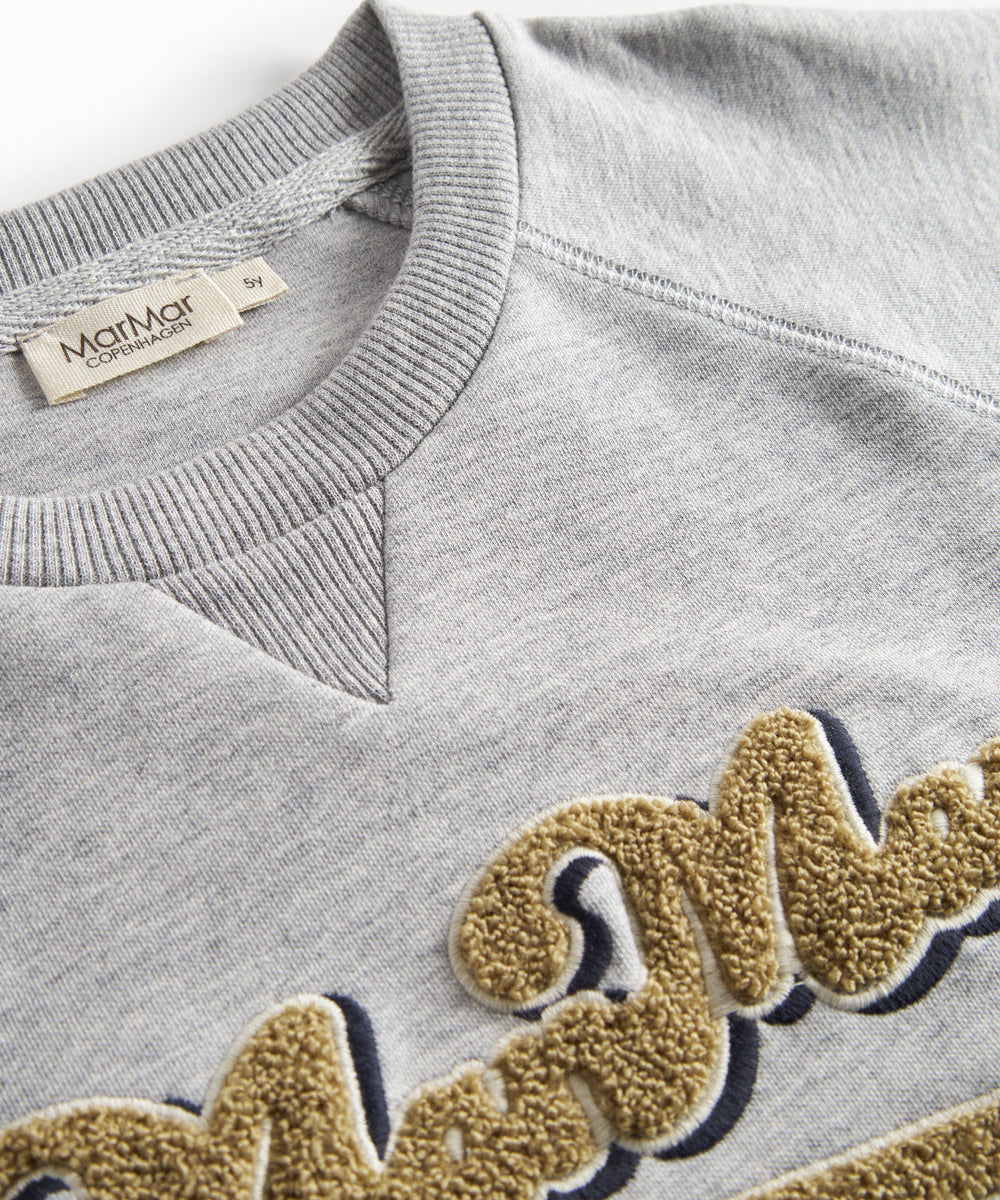 Nærbillede af gyldent broderi på grå sweatshirt til børn