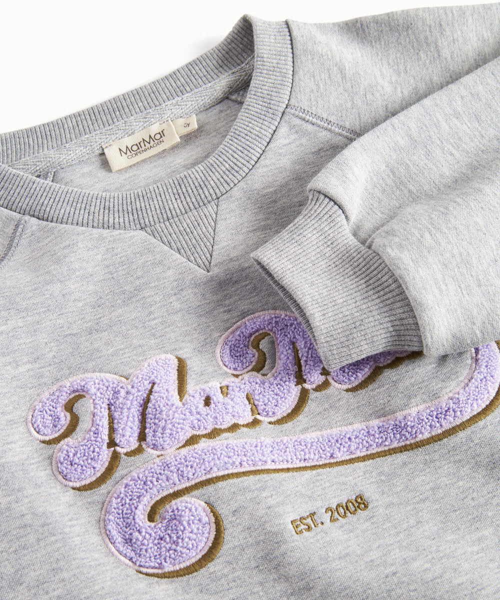 Nærbillede af lila broderet logo på grå sweatshirt til børn