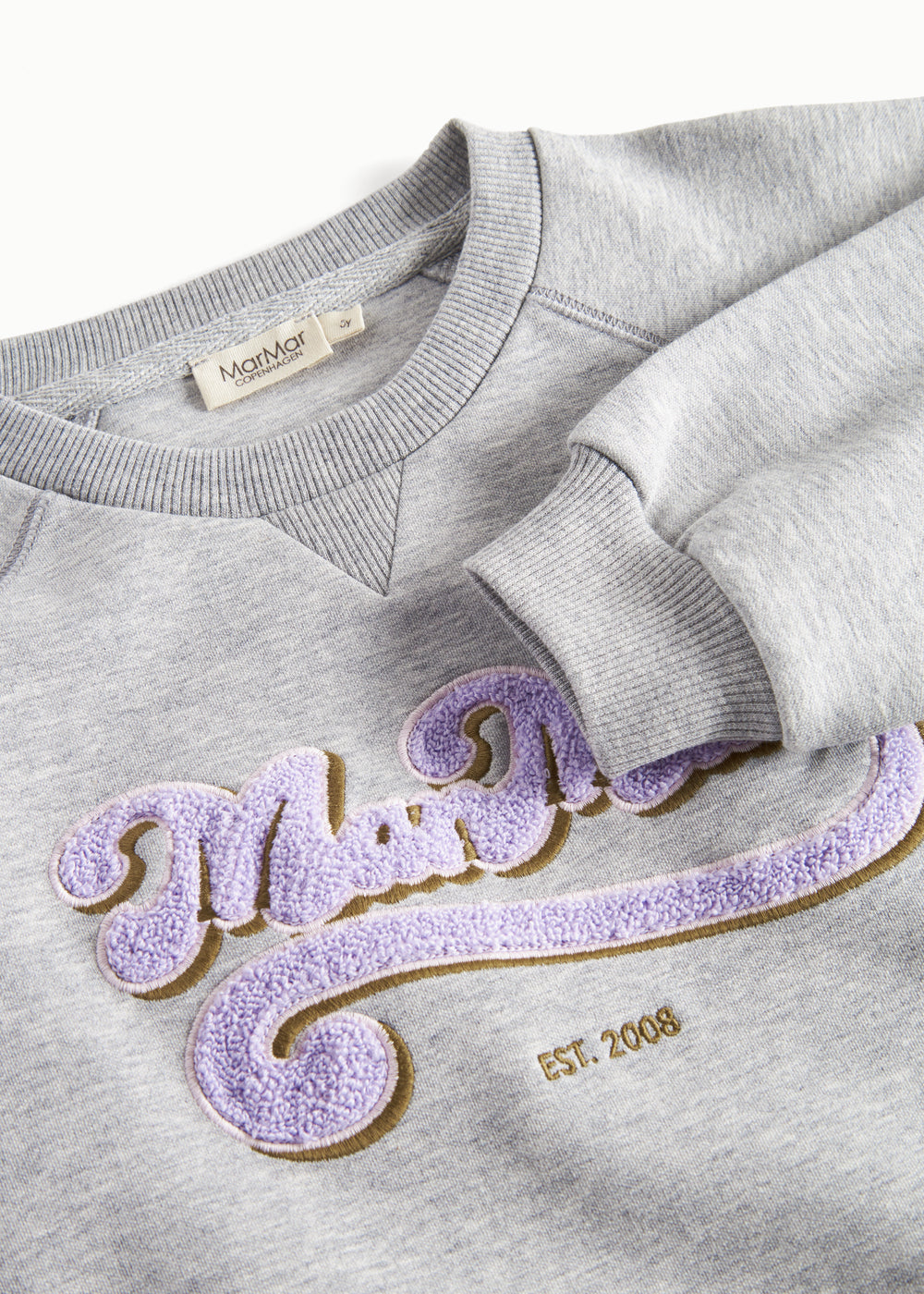 Nærbillede af lila broderet logo på grå sweatshirt til børn