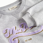 Nærbillede af lila broderet logo på grå sweatshirt til børn
