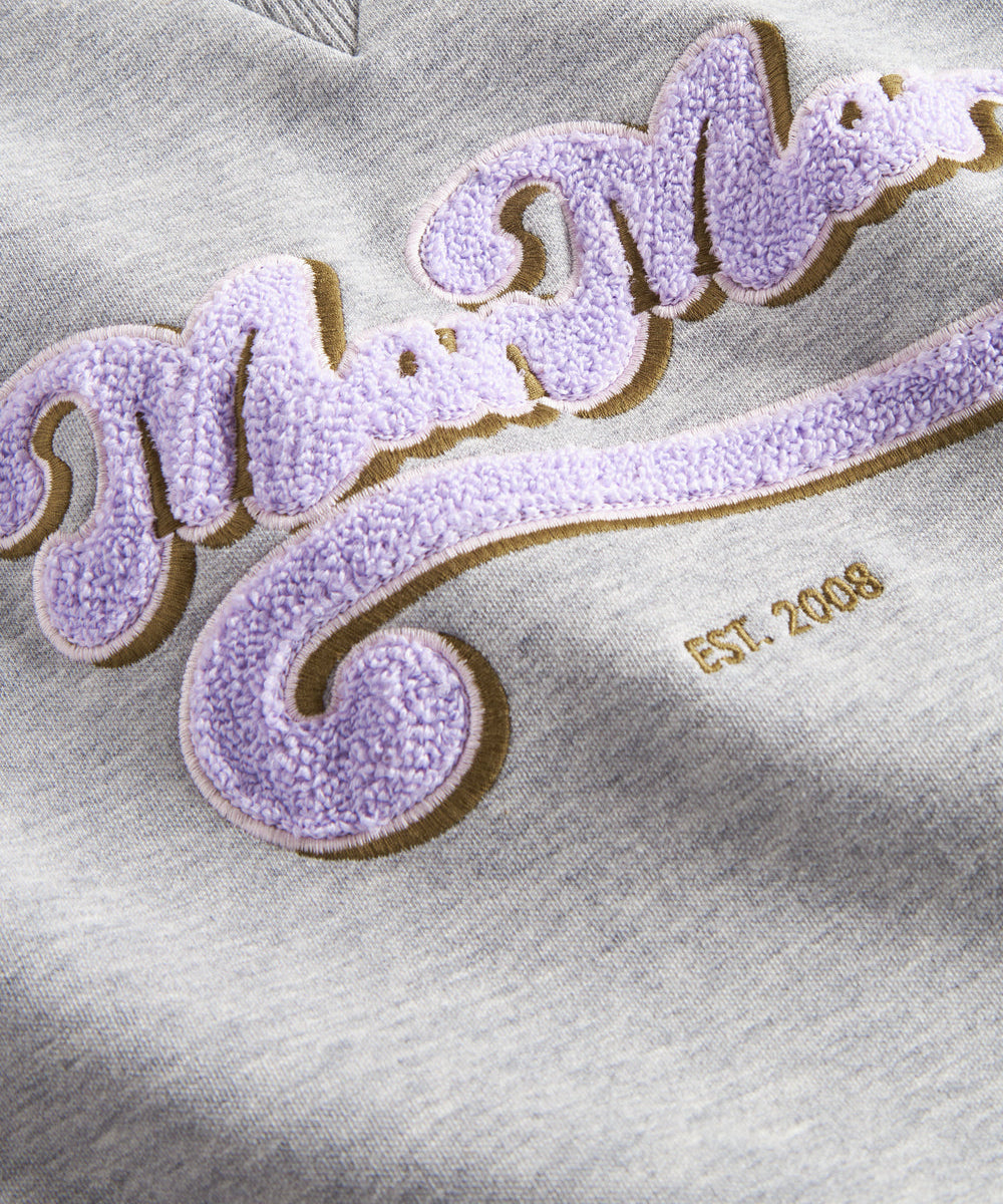 Nærbillede af lila broderet logo på grå sweatshirt til børn