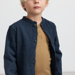 Dreng iført mørkeblå skjorte over brun t-shirt