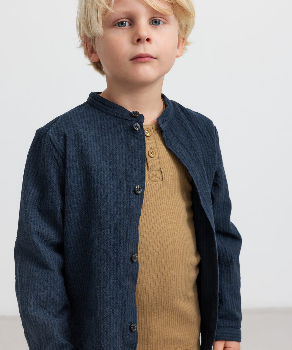 Dreng med blå jakke og brun ribstrikket langærmet t-shirt