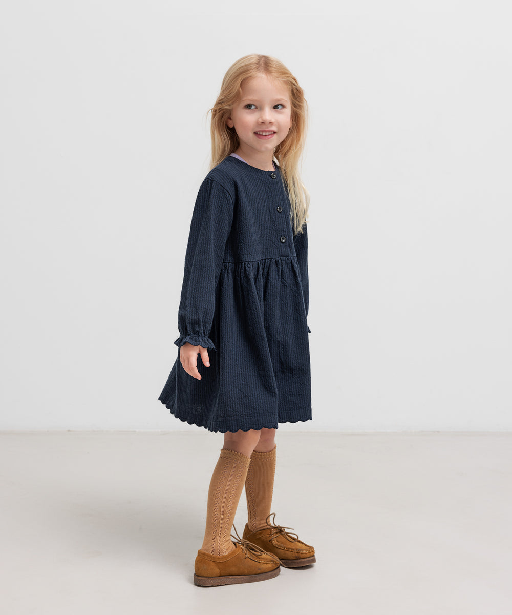 Pige iført mørkeblå kjole med rynket talje 