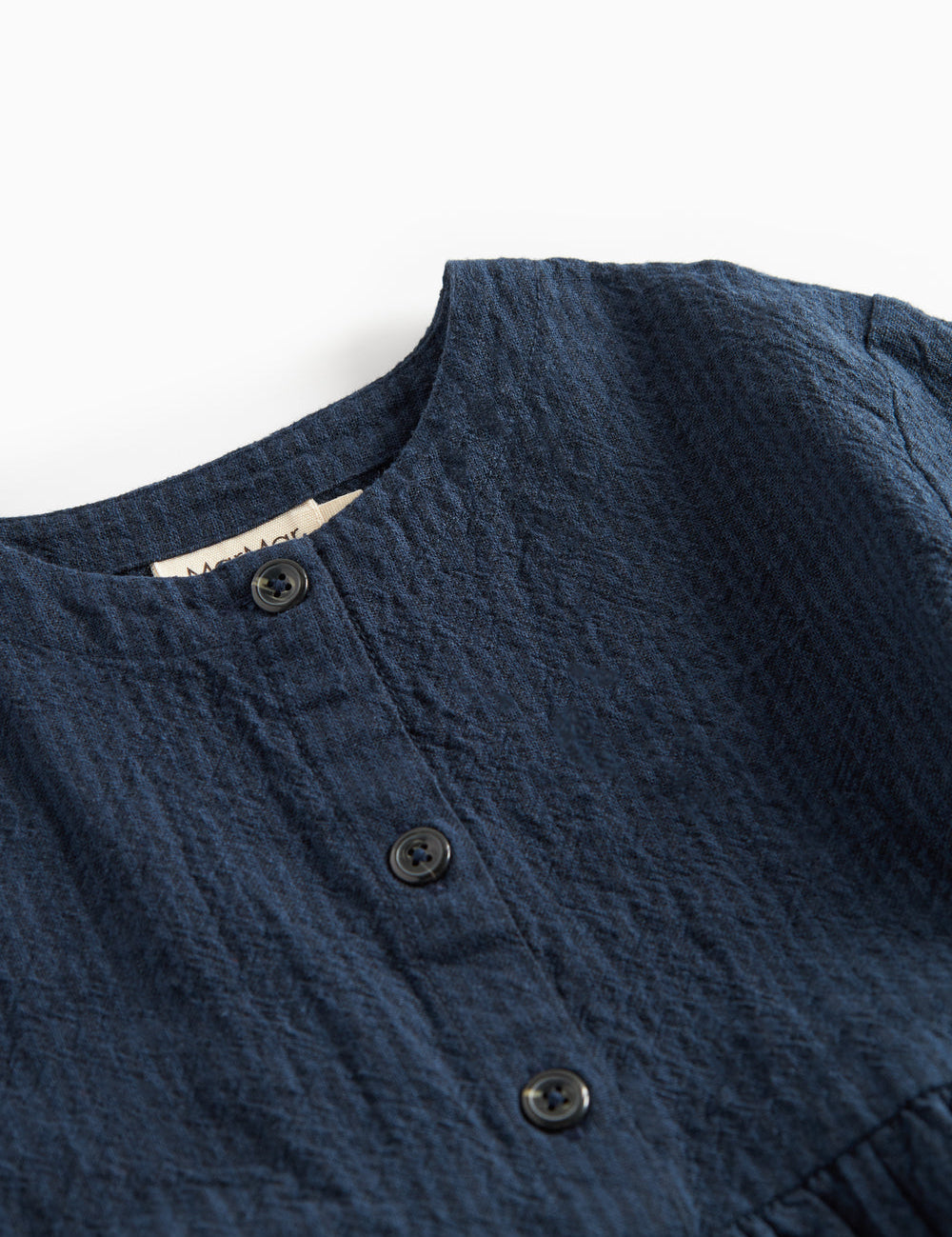 Detaljebillede af knapper og stofstruktur på mørkeblå kjole