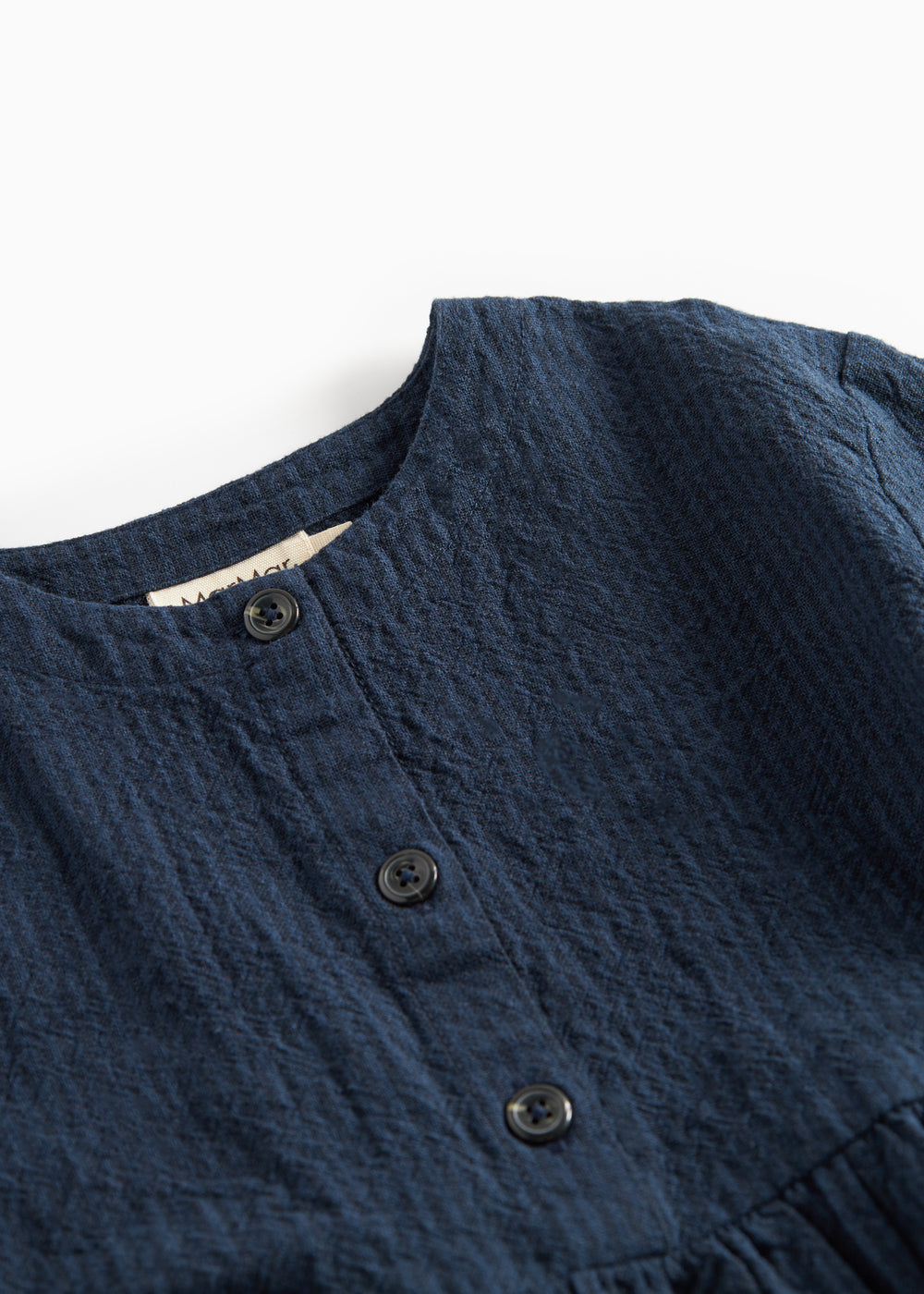 Detaljebillede af knapper og stofstruktur på mørkeblå kjole