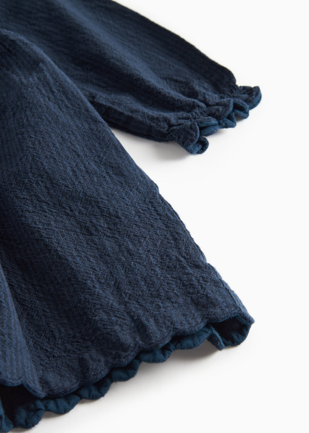 Detaljebillede af ærmekant med bølget afslutning på mørkeblå kjole