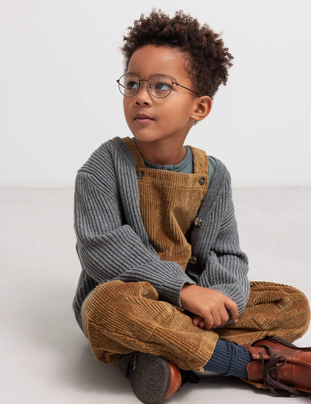Boy wearing brown velvet jumpsuit and gray cardigan