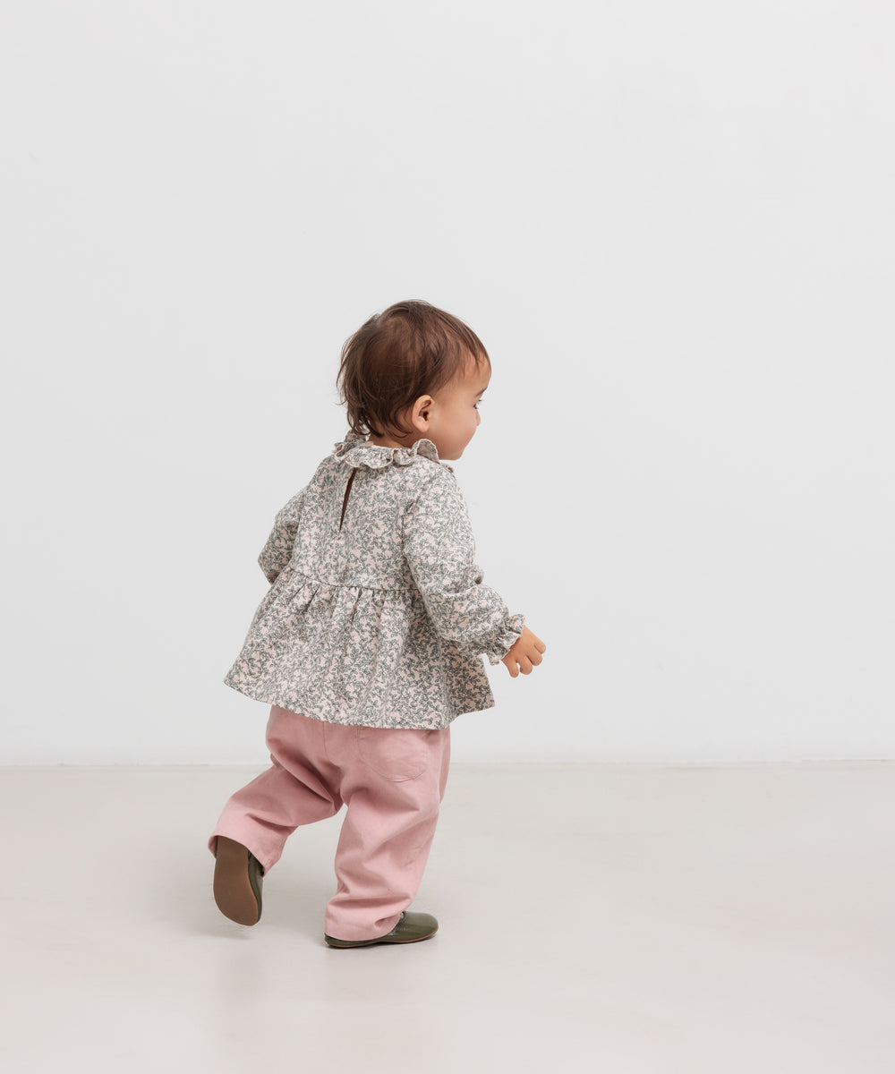 Baby iført lyserøde bukser og grå bluse set bagfra