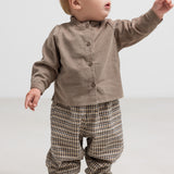 Baby iført beige babyfløjlsskjorte og ternede bukser