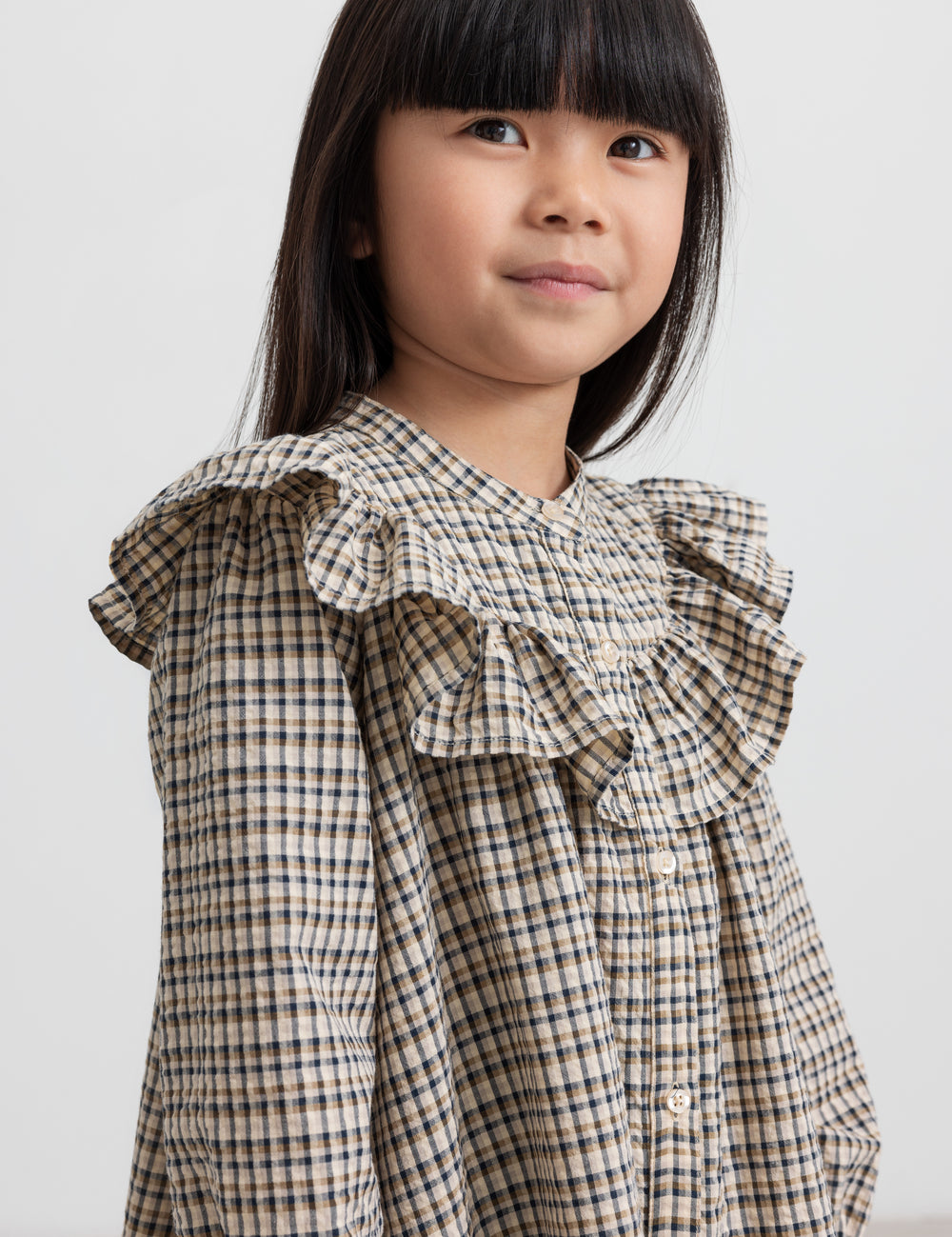 Pige iført brun ternet strikkjole med flæser foran