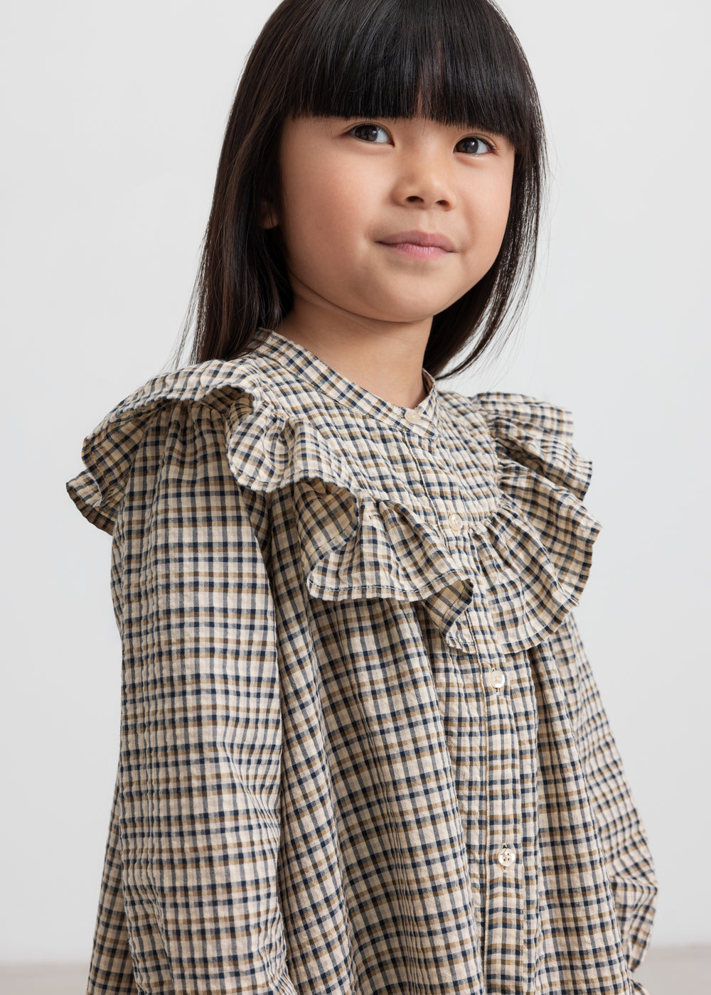 Pige iført brun ternet strikkjole med flæser foran