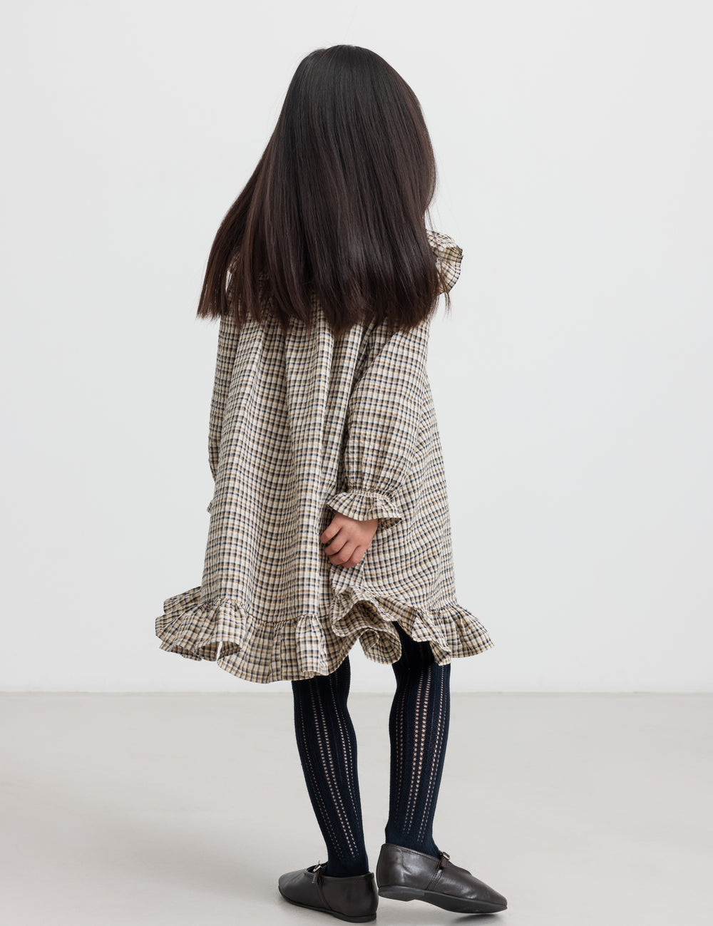 Pige iført brun ternet strikkjole med flæser foran