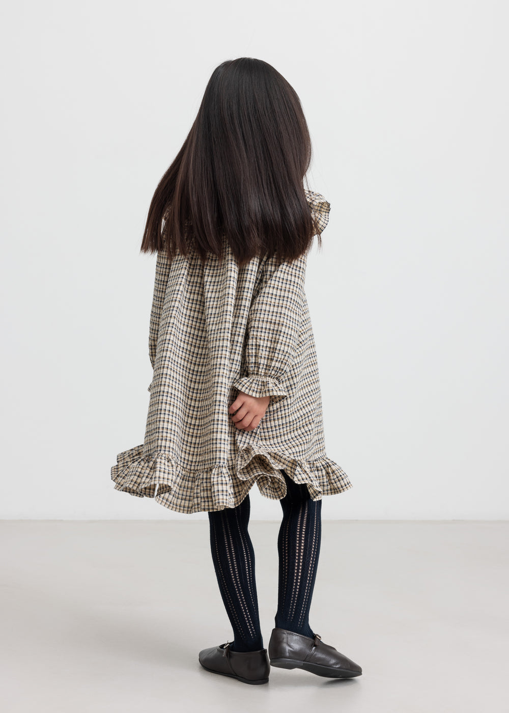 Pige iført brun ternet strikkjole med flæser foran