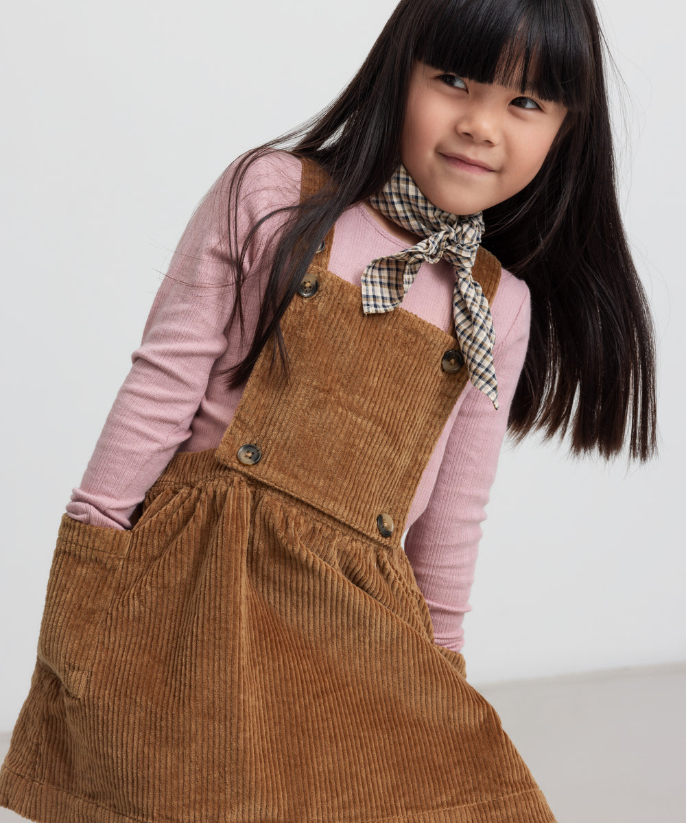 Pige iført brun fløjlssele­kjole og lyserød bluse