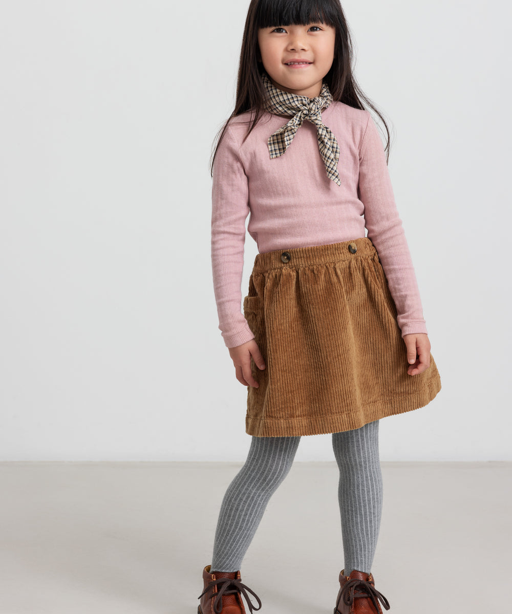 Pige iført rosa pointelle bluse og brun nederdel