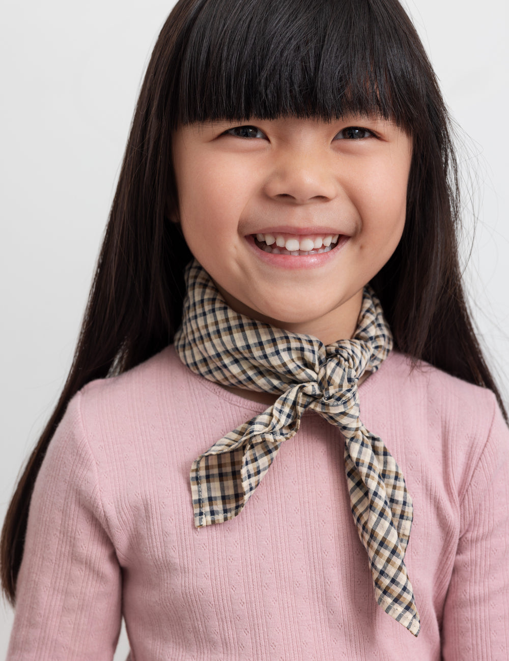 Pige med brun ternet tørklæde bundet om halsen og lyserød t-shirt