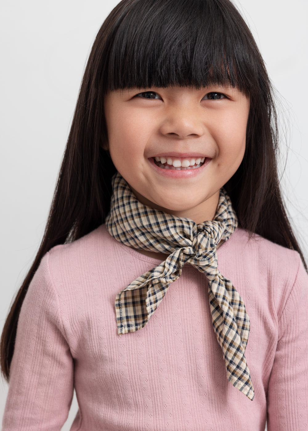 Pige med brun ternet tørklæde bundet om halsen og lyserød t-shirt