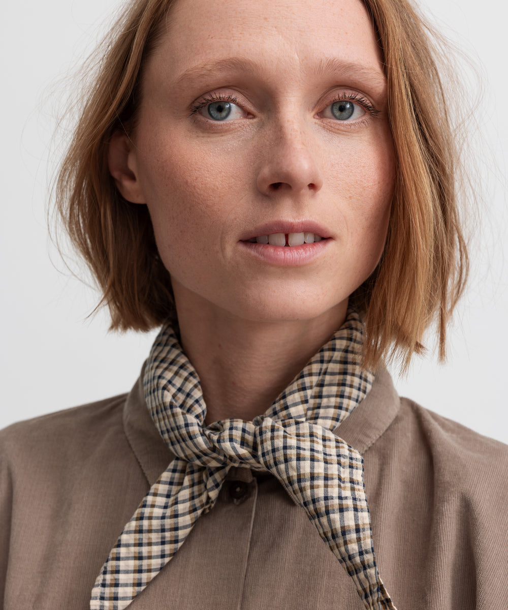 Kvinde i beige skjorte med ternet tørklæde om halsen