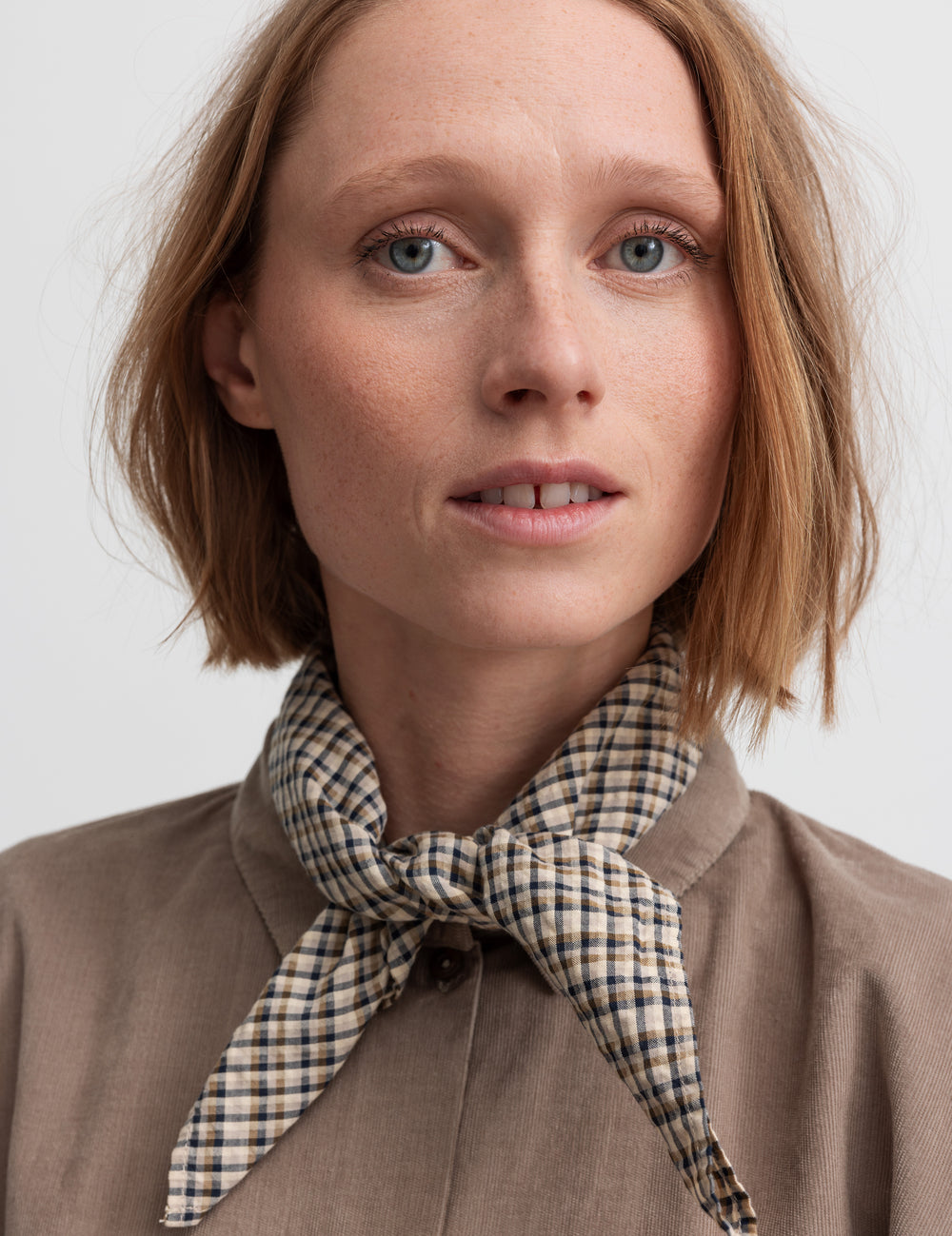 Kvinde i beige skjorte med ternet tørklæde om halsen