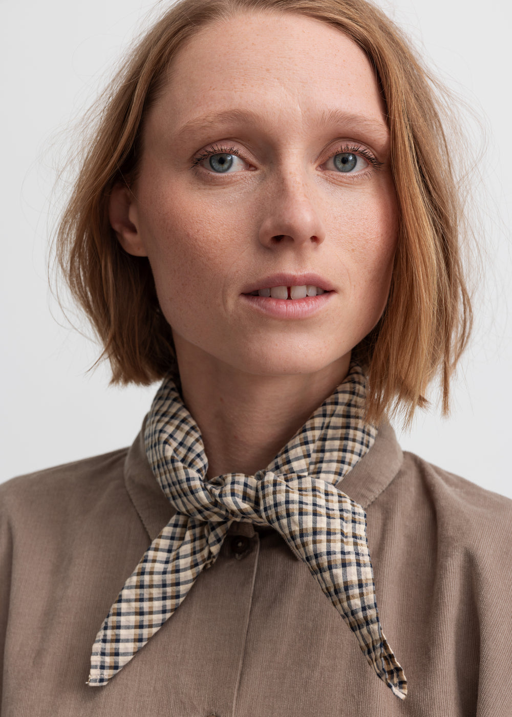 Kvinde iført brun ternet tørklæde bundet om halsen
