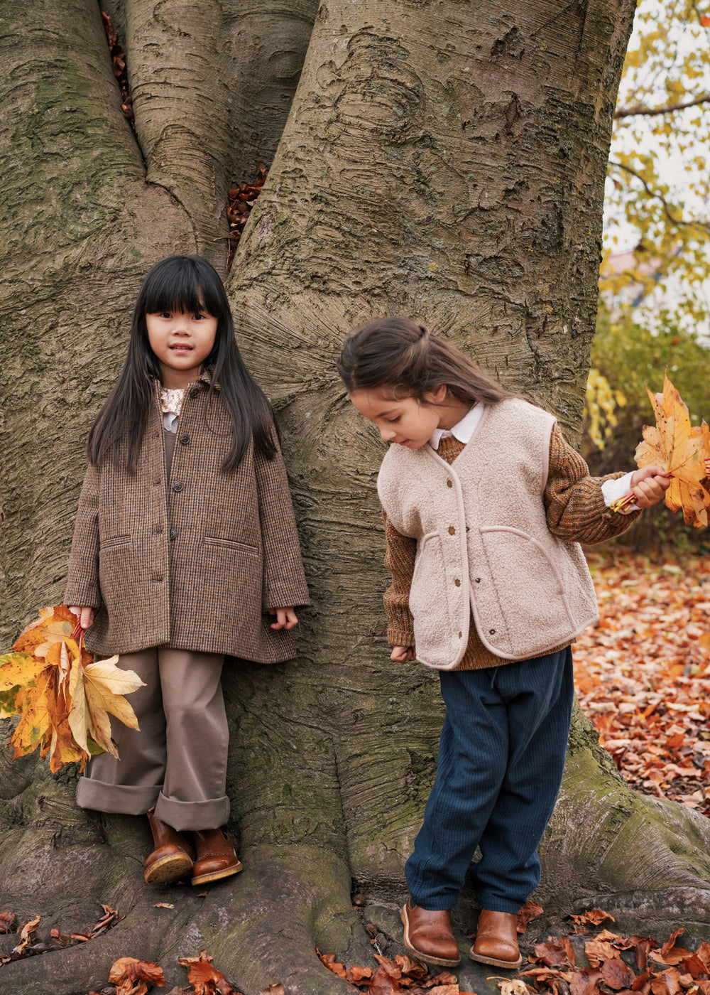 To piger i efterårstøj leger ved et træ ude i naturen