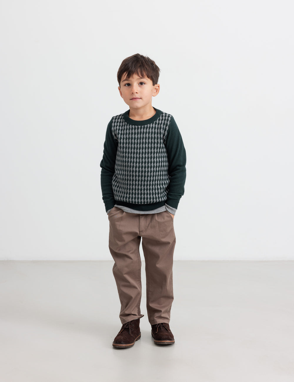 Dreng iført mørkegrøn strikket bluse med ternet mønster og brune bukser til børn