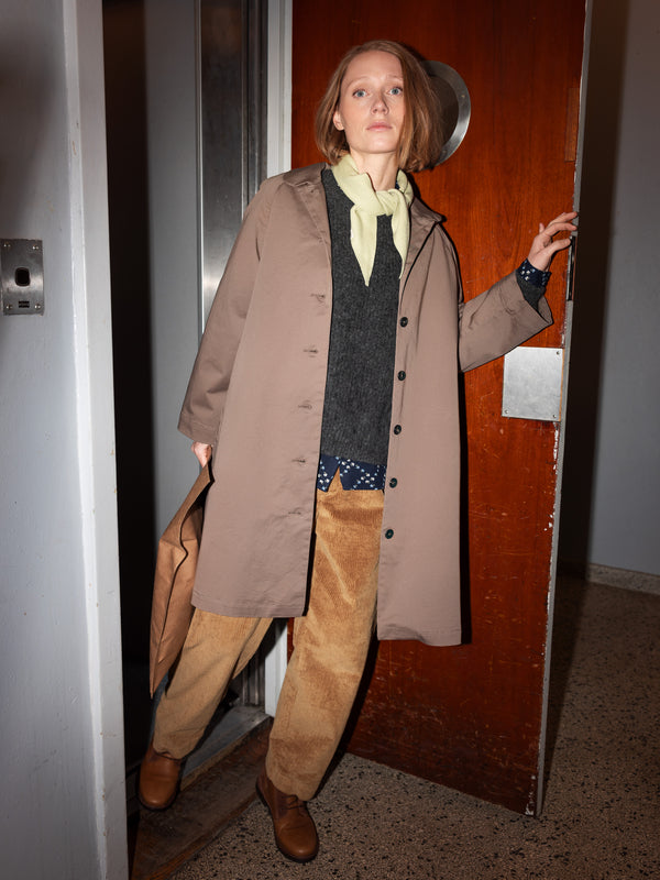 Kvinde iført beige frakke, mørk trøje og fløjlsbukser