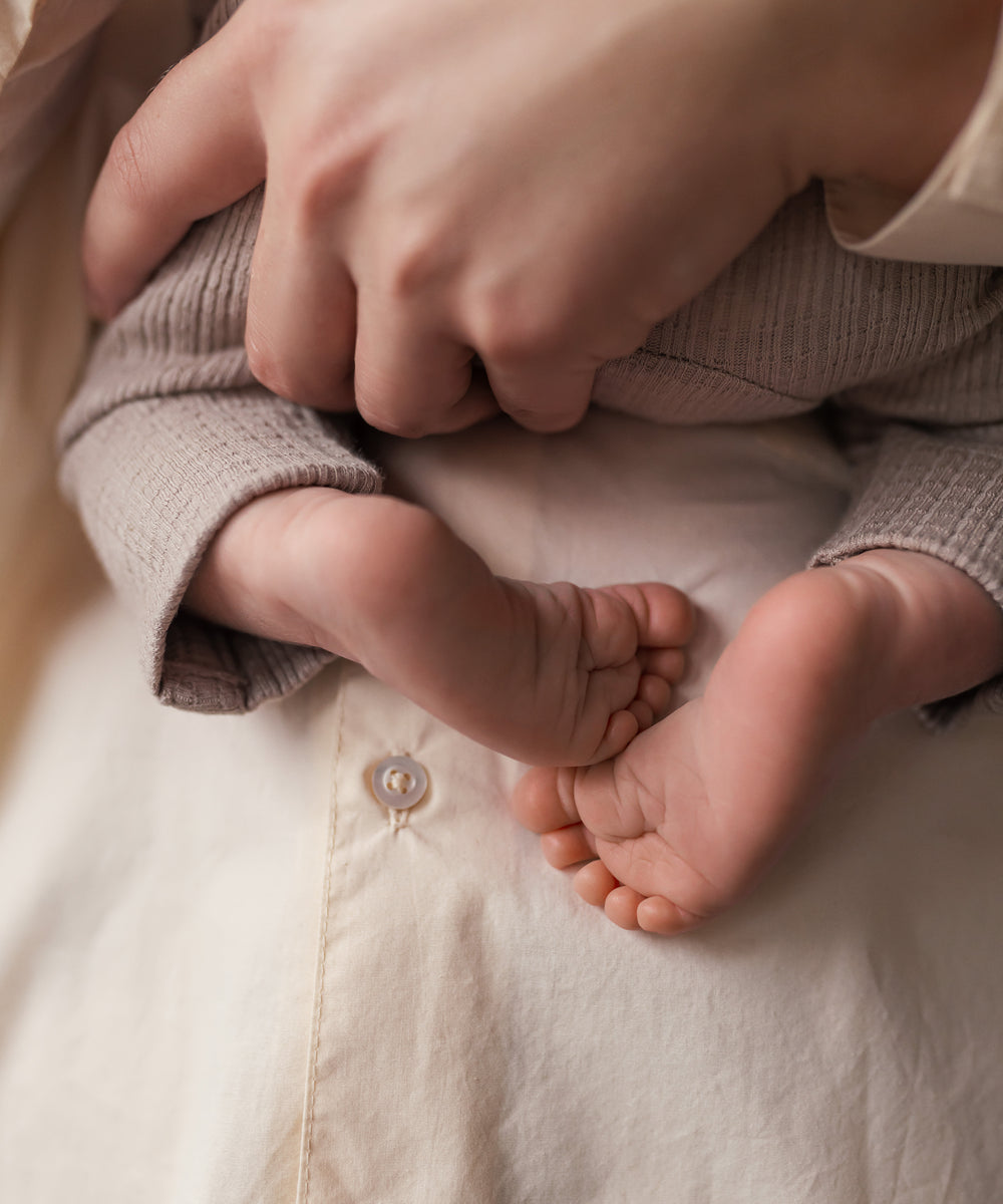 Mor holder nyfødt iført beige pointelle hue og sparkedragt