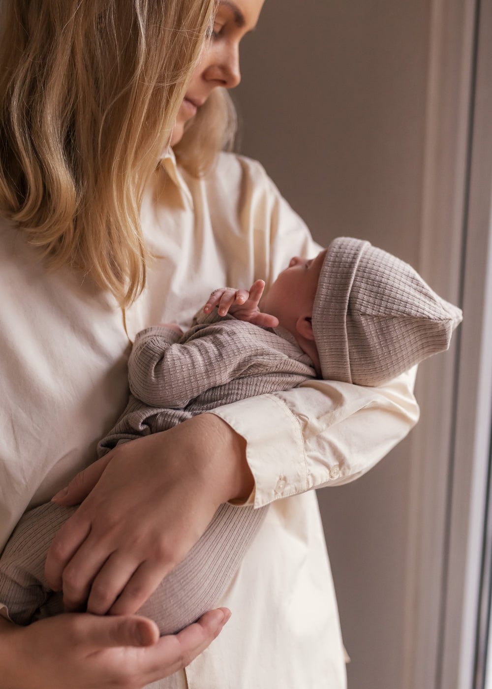 Mor holder nyfødt iført beige pointelle hue og sparkedragt