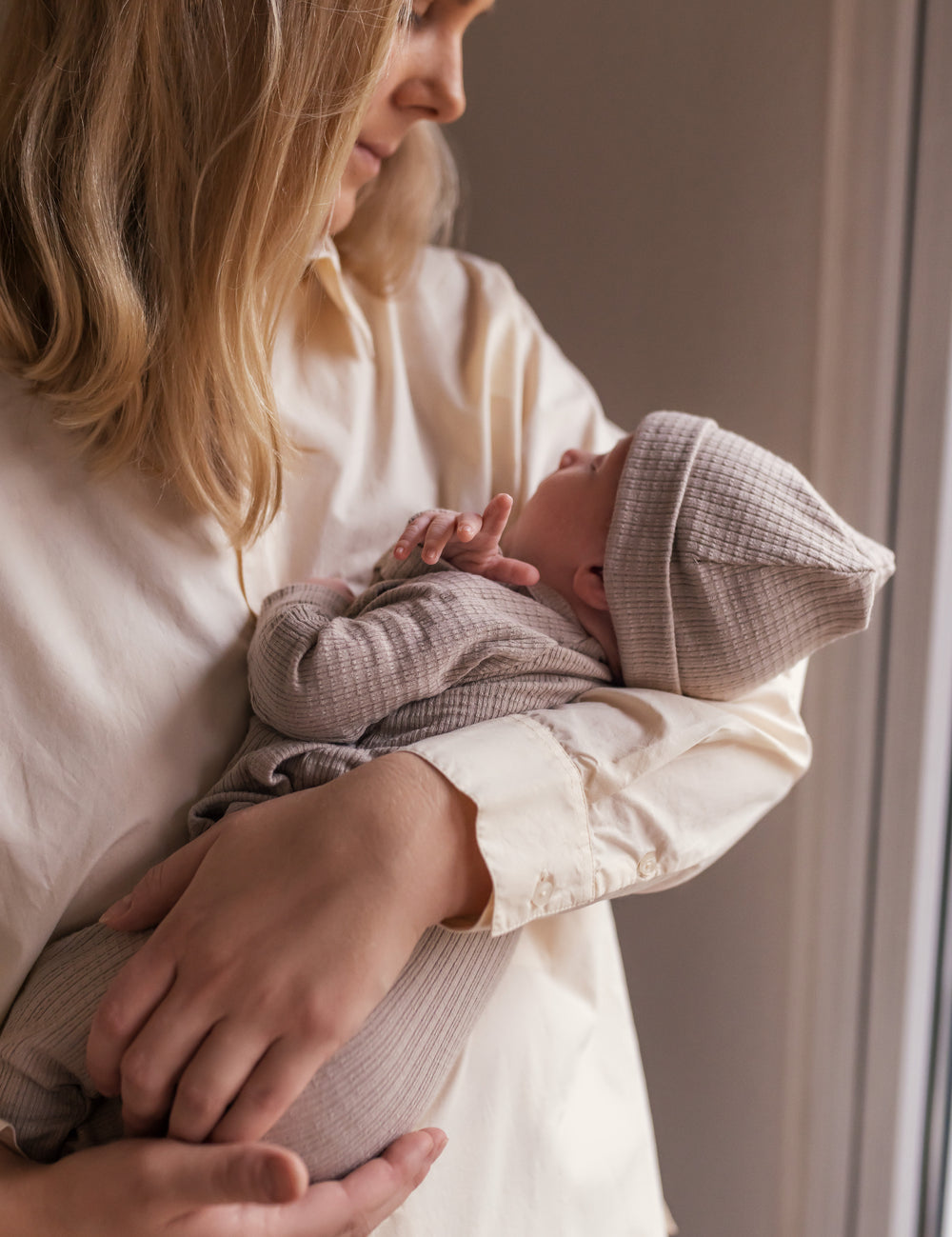 Mother holding newborn wearing beige pointelle hat and romper