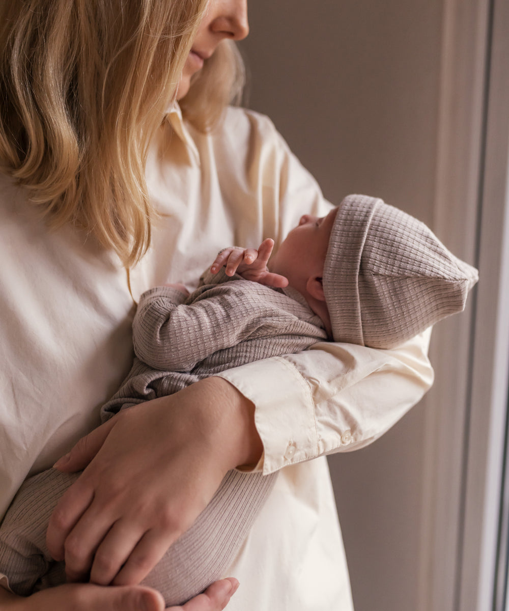Mor holder nyfødt iført beige pointelle hue og sparkedragt