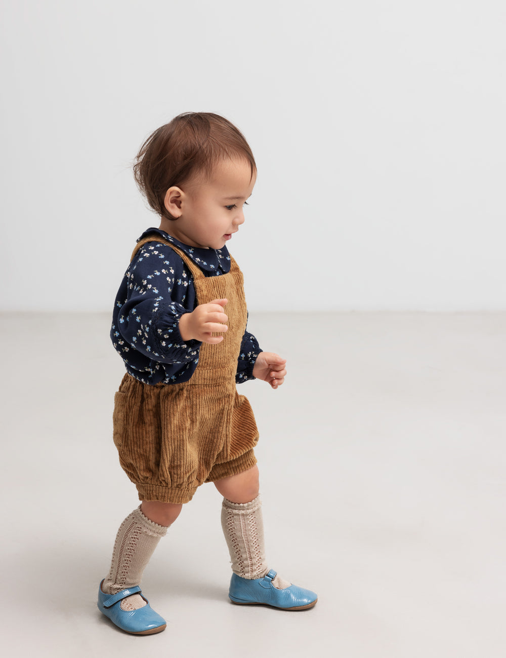 Baby wearing brown corduroy shorts with suspenders and dark blue blouse