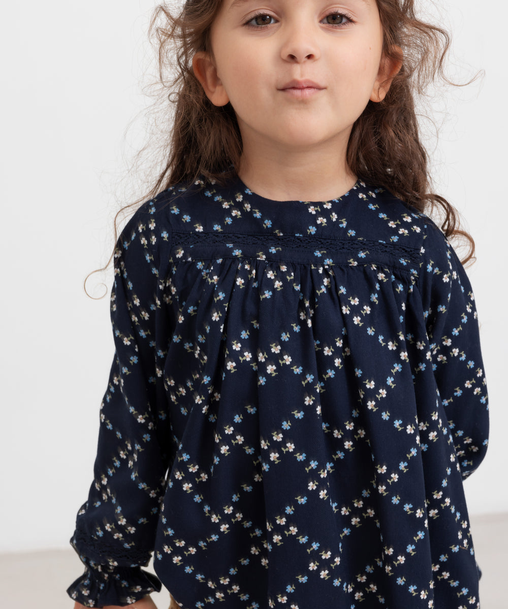 Pige iført mørkeblå blomstermønstret bluse med lange ærmer