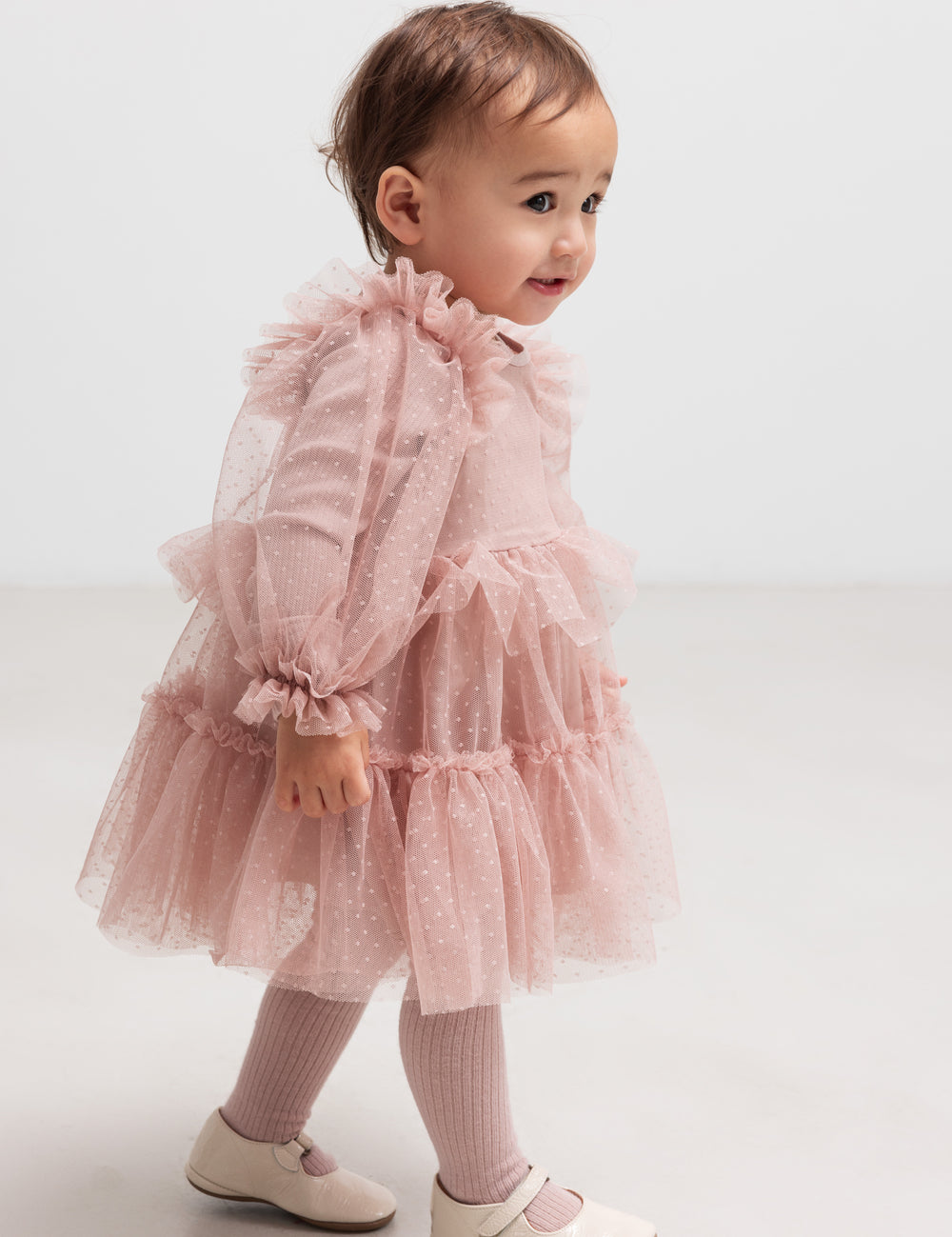 Little child in pink tulle dress with ruffles and long sleeves