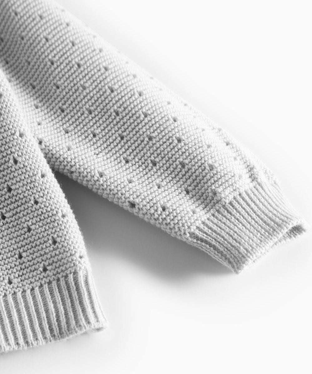 Detalje af ærme med hulmønster på grå strikbluse