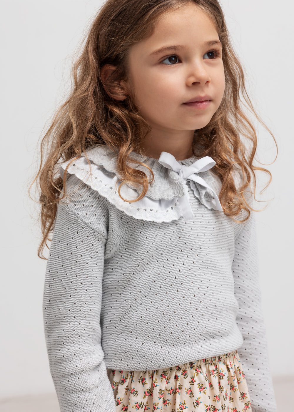 Pige med grå strikbluse med flæsekrave og mønstret nederdel