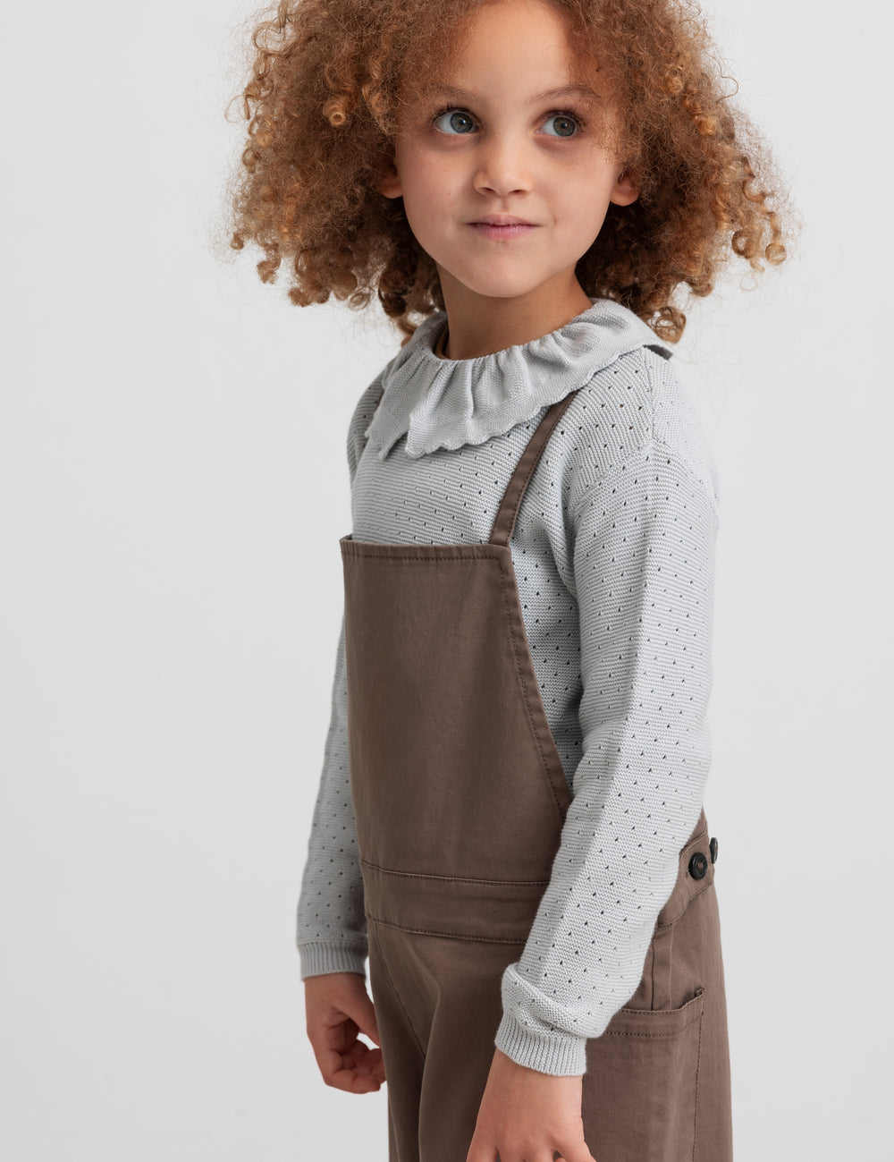 Girl wearing brown suspenders and gray knit blouse, front view